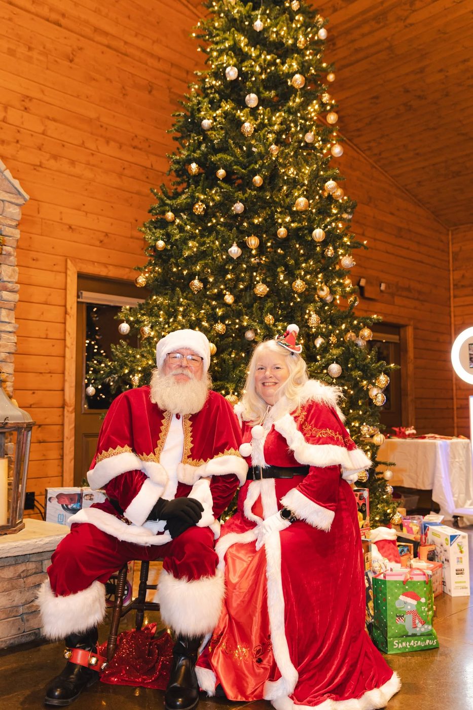 Santa and Mrs. Claus in front of a lit Christmas tree with gifts