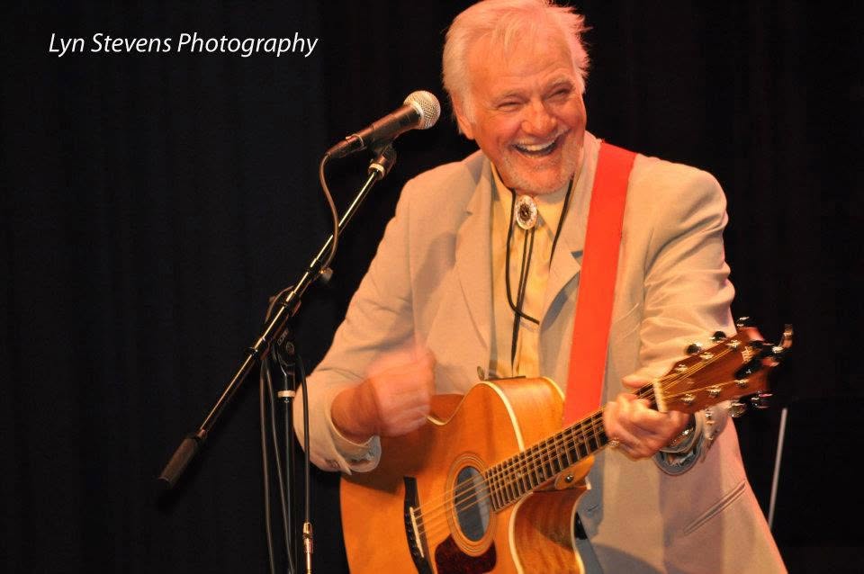 Jerry Foster singing and playing acoustic guitar on stage