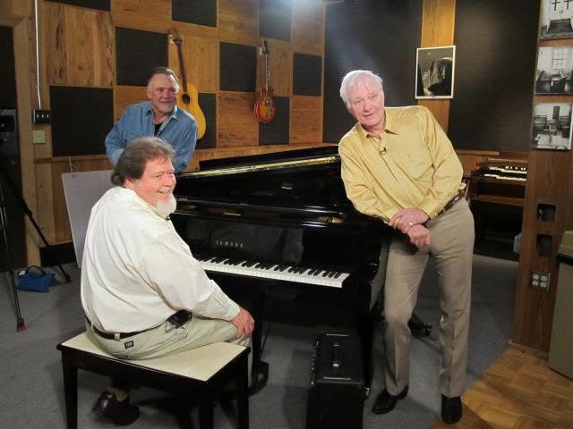Jerry Foster standing by a grand piano in a studio with two other men