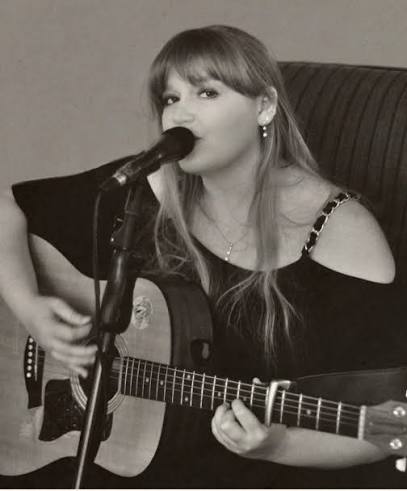 Black and white photo of Olivia West singing with an acoustic guitar