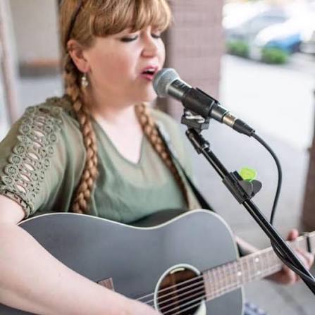 Olivia West singing and playing acoustic guitar